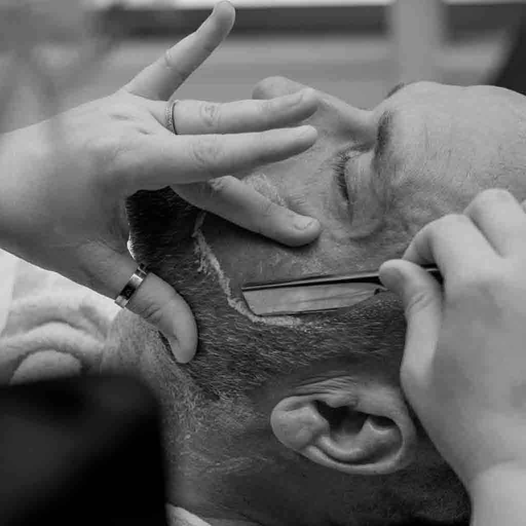 In a classic barbershop moment, a skilled barber in Toowoomba is captured carefully shaving a customer with precision. This image encapsulates the traditional barber experience, highlighting quality men's haircuts and grooming services available near you.