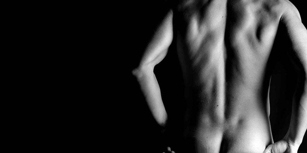 A monochromatic image highlighting the defined torso of a man from a side perspective, exemplifying the transformation from 'Bare to Bold' at Core Benefits Toowoomba with services like barbering, massage, waxing, laser treatments, and men's skin treatments to foster confidence and self-improvement.