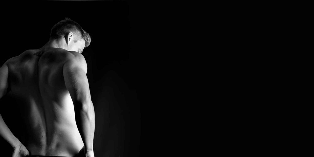 Black and white image capturing the strong back muscles of a man looking away, highlighting Core Benefits Toowoomba's commitment to helping men achieve their best self with services like barbering, massage, waxing, and laser treatments that inspire 'Bare to Bold: Effortless Confidence Begins Here'.